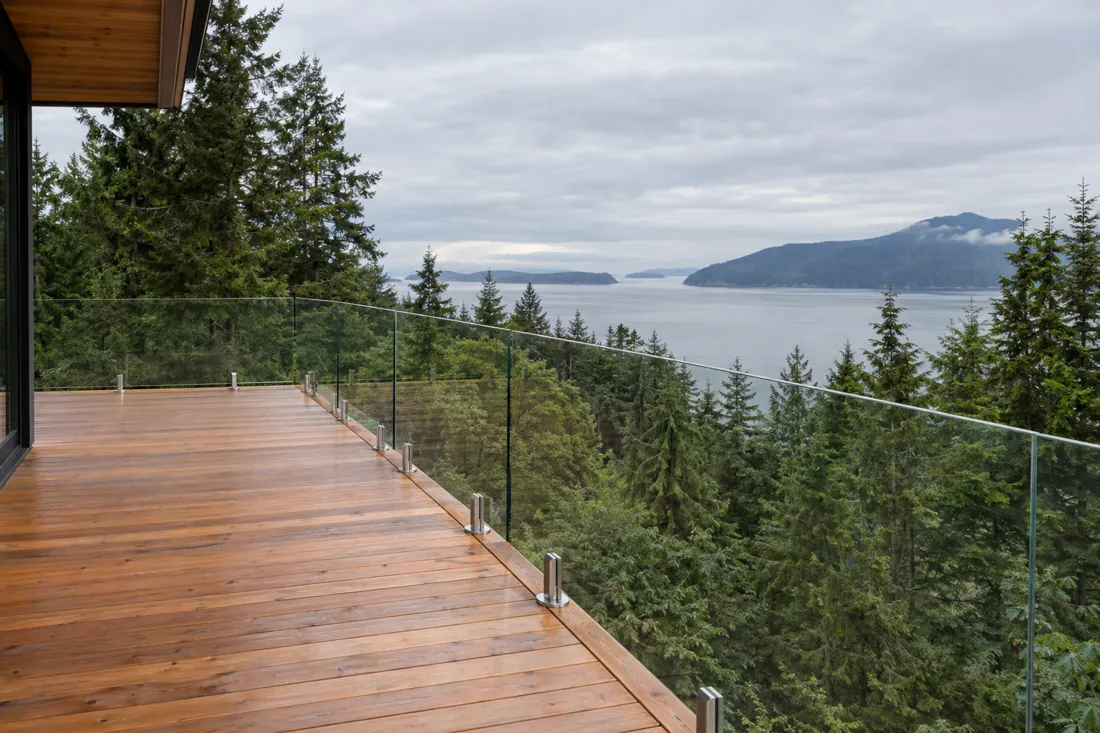 Cedar deck with a frameless glass railing overlooking evergreen forest and water
